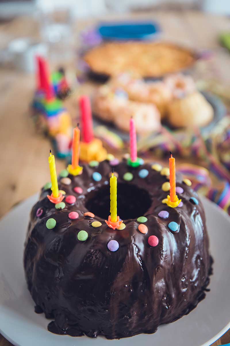Ein Geburtstagskuchen steht auf einem Tisch. Auf dem Kuchen sind bunte Kerzen.